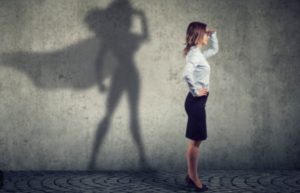 Woman standing in front of a wall. The shadow on the wall portrays a superhero silhouette.